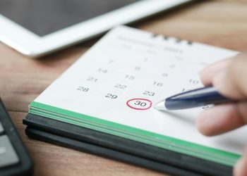 Close-up shot of a hand marking a date on a calendar with a pen, emphasizing planning and scheduling.