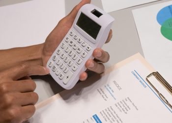 Close-up of hands using a calculator next to a company invoice, depicting a financial calculation concept.